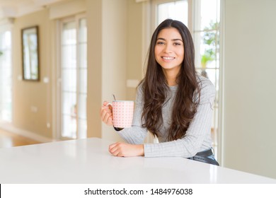 Young woman drinking a cup of coffee with a happy face standing and smiling with a confident smile showing teeth
