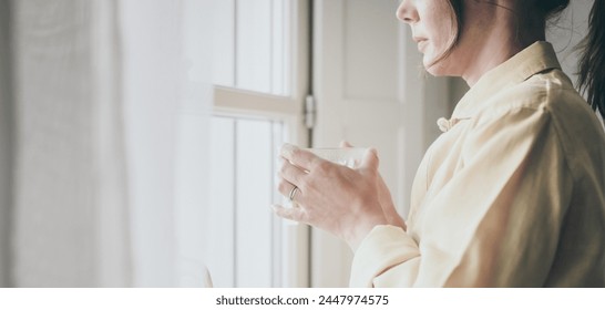 Young woman drinking a cup of tea looking outside the window Portrait of a girl enjoying free time at home. Middle aged female with a drink in the hand look through the door. Lifestyle leisure concept - Powered by Shutterstock