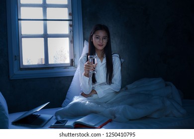 Young Woman Drinking Glass Of Water In Bed At Night