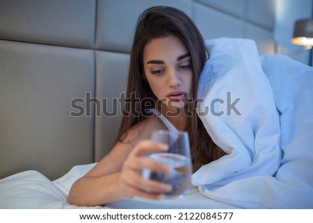 Young woman drinking glass of water in bed at night. Woman drinking a glass of water before going to sleep, she is lying in bed