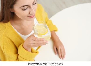 Young Woman Drinking Lemon Water At White Table, Above View