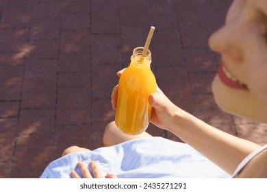 Young woman drinking orange juice from a glass mockup jar with a paper tube while sitting outside, rear view. The concept of chatting with friends and spending time, responsible consumption - Powered by Shutterstock