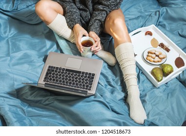 Young woman drinking tea at home in her bed and checking her laptop, top view