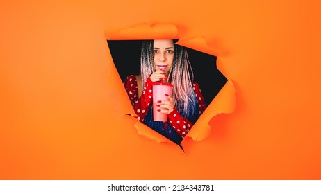 Young woman drinking through soft drink straw in hole of orange background. Bright lady enjoying nonalcoholic beverage - Shutterstock ID 2134343781