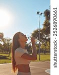 Young woman drinking water after jogging and exercise in urban park.