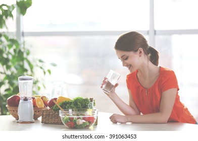 Young Woman Drinking Water Near Table With Fruits And Vegetables In The Kitchen