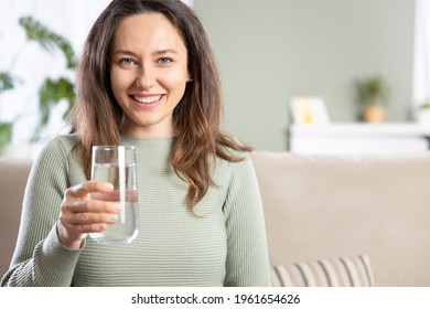 Young Woman Drinking Water Sitting On A Couch At Home. Health Benefits Of Drinking Enough Water Concepts. 