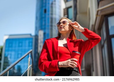 A Young Woman Drinks Coffee On The City Streets Of A Metropolis In Autumn Or Early Spring. Business Woman Concept