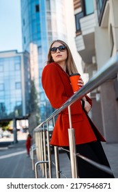 A Young Woman Drinks Coffee On The City Streets Of A Metropolis In Autumn Or Early Spring. Business Woman Concept