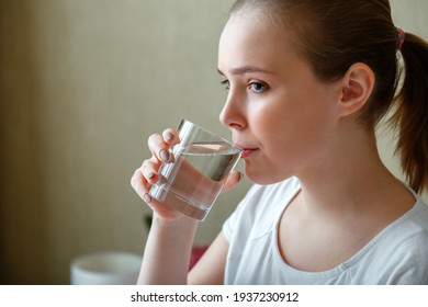 Young Woman Drinks Glass Of Pure Water In Morning After Waking Up. Happy Teen Girl Maintains Water Balance For Body Health By Drinking A Transparent Cup Of Clean Water