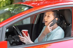 A Young Woman Driver In A Car With A Cup Of Coffee In Her Hands Speaks On A Mobile Phone.