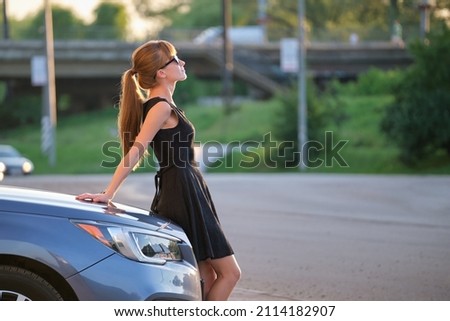 Young woman driver enjoying warm summer day standing beside her car on city street. Travelling and vacation concept