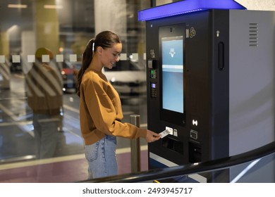 Young woman driver paying for ticket in parking meter near terminal in the underground parking area