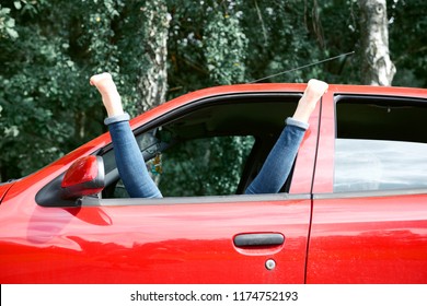young woman driver resting in a red car, put her feet on the car window, happy travel concept