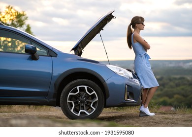 Junge Autofahrerin, die in der Nähe eines defekten Autos steht, mit aufgetauchter Motorhaube, die auf Hilfe wartet.