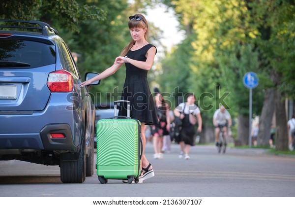 Young woman driver taking out suitcase\
bag out of her car. Travelling and vacations\
concept