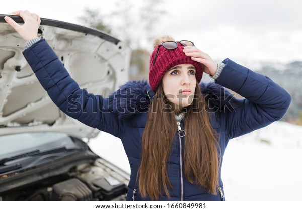 Young woman driver under stress next to\
broken car with opened hood. Winter\
scene.