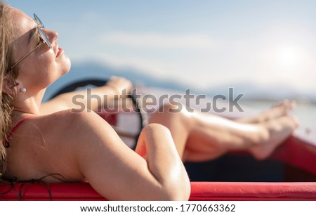 young woman drives a rental boat over the Chiemsee on a beautiful sunny day and sunbathes