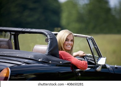 A young woman driving a black sports car