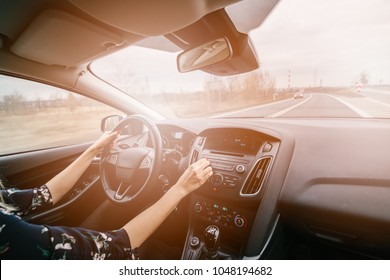 Young Woman Driving A Car And Adjusting Car Audio. Music In A Car. Sunny Day. Modern Car Interior