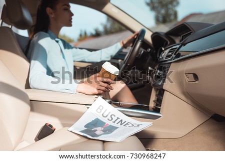 Young woman driving a car with business newspaper lying in front seat