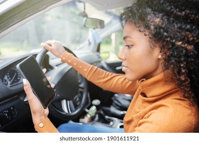 Young woman driving car and checking her phone.