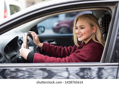 Young woman driving a car in the city. Portrait of beautiful woman in a car, looking out of the window and smiling. Travel and vacations concepts