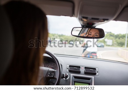 Young, woman driving a car, going home from work, fixing her make-up, checking herself in the rearview mirror