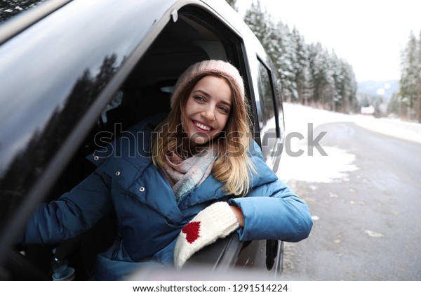 Young woman driving car and looking out of\
window on road. Winter\
vacation
