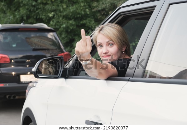 Young woman driving a car\
stuck her head out the window and showing middle finger. Angry\
woman with blond hair demonstrating fuck you off sign from open\
window.