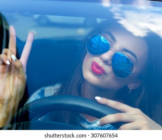 Young woman driving her car.Stylish student girl in car.Summer fashion close up portrait elegant beautiful woman driving her car in urban city.Funny Female driver in swag sunglasses and red lipstick