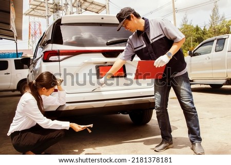 Young woman driving rookie driver sit hold cash nervously looking at her new red registered damaged car in the back while having mechanic make an appraisal for the costlycostly car insurance analysis.
