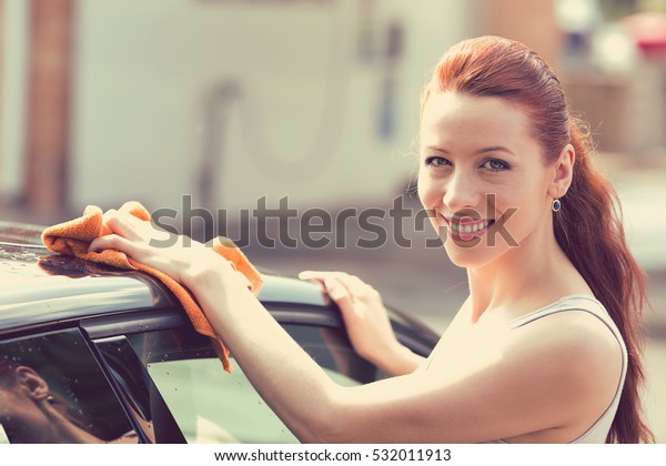 Young woman dry wiping her car with\
microfiber cloth after washing it, cleaning auto. Transportation\
self service, care concept. Paint color\
protection