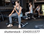 Young woman during grueling workout with dumb-bell in sports hall of fitness club. Intense exercise, increased endurance. Group and personal training, development of individual couching programs