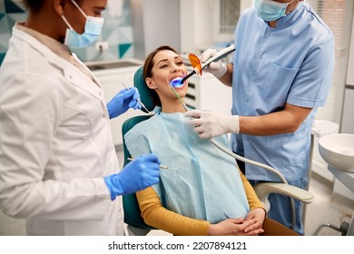 Young woman during teeth whitening procedure with curing UV light at dentist's office.