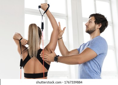 Young woman during workout with a personal fitness instructor using rubber  resistance bands in the gym.