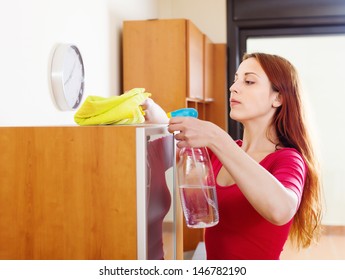 Young Woman Dusting Wooden Furniture With Rag And Cleanser At Home