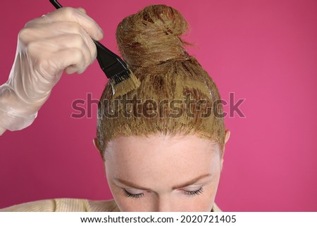 Young woman dyeing her hair with henna on pink background, closeup