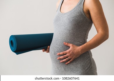 Young Woman In Early Pregnancy With Rolled Mat Under Her Arm Going To Prenatal Yoga Class