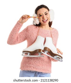 Young woman in earmuffs with ice skates and candy cane on white background