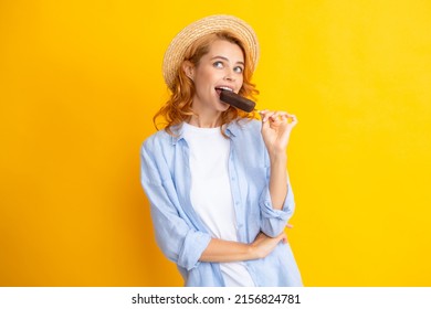 Young woman eat ice creams with chocolate glaze on yellow background. Funny redhead girl with summer straw hat lick ice cream.
