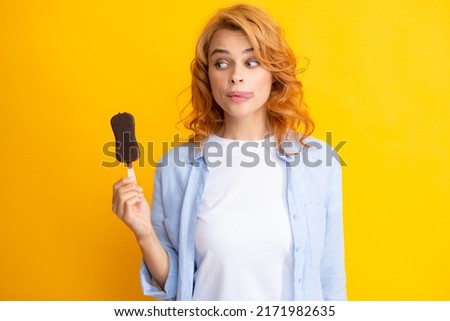 Young woman eat ice creams with chocolate glaze on yellow background. Funny redhead woman with ice cream. Licking lips.