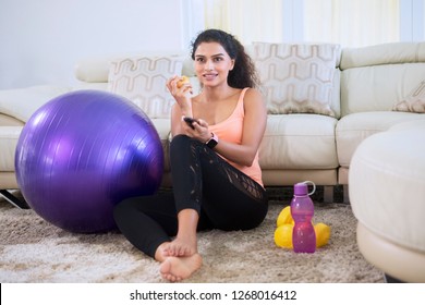 Young woman eating an apple while watching television after exercising at home
