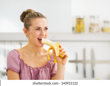 Young Woman Eating Banana In Kitchen