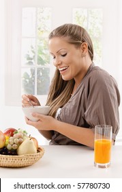 Junge Frau, die Frühstücksflocken und Orangensaft trinkt, lächelt.