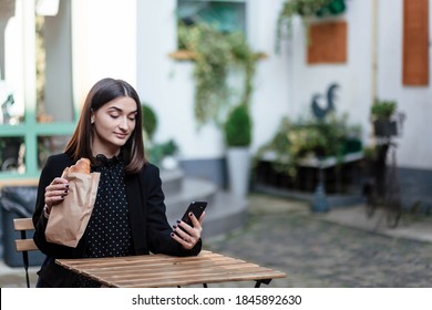 Young Woman Eating Breakfast And Smiling, Eating Croissants And Talking On The Phone. She Is Talking To Someone On A Cell Phone. Breakfast.