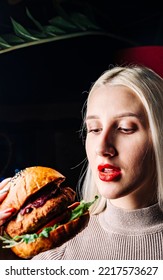 Young Woman Eating Burger In Hands On Black Background