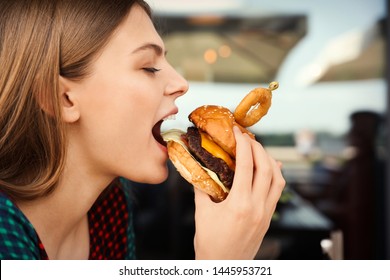 Young Woman Eating Burger In Street Cafe