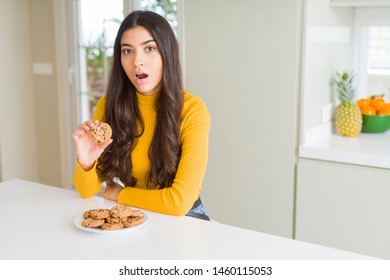 Junge Frau, die zu Hause Schokoladenkekse isst, hat Angst vor Schock mit einem überraschenden Gesicht, Angst und aufgeregt mit Angst vor Ausdruck