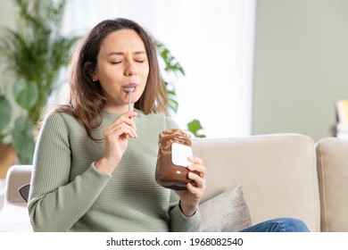 Young woman eating chocolate from a jar at home
